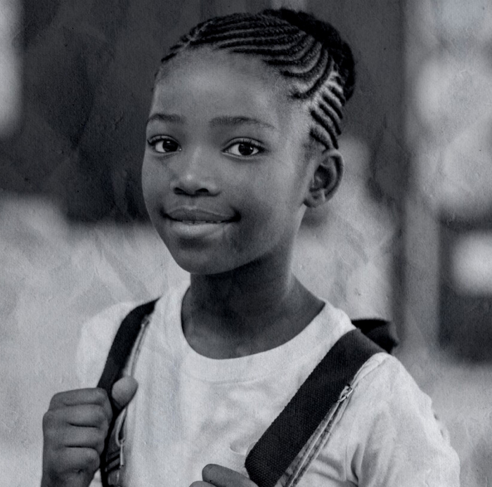 A young girl with braided hair smiles at the camera while holding the straps of her backpack, embodying the vibrant spirit of an adolescent who benefits from the support of a dedicated équipe mobile focused on mental health.